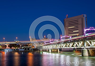 Train crossing a railway bridger over a river in Tokyo at night Stock Photo