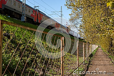 The train passes along the fence of the park Stock Photo