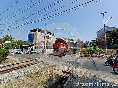 A Train with a Red and Blue Locomotive Crossing a Crowded Road Editorial Stock Photo