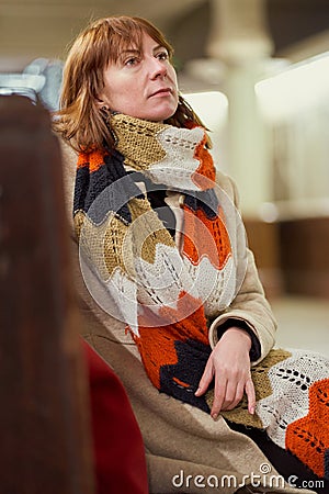 Train Station. Mature woman in warm clothes is sitting in waiting room and waiting for train. Evening is dark. Vertical Stock Photo