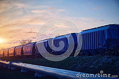 Train with wagons loaded with grain moves at sunset along the pipeline Stock Photo