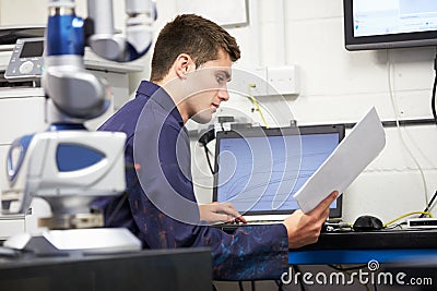 Trainee Engineer Studying Plans With CMM Arm In Foreground Stock Photo