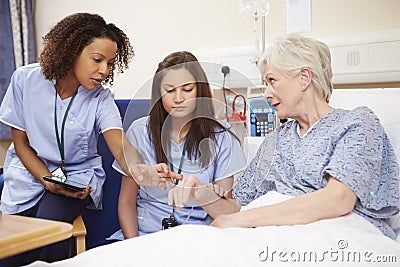 Trainee Nurse Sitting By Female Patient's Bed In Hospital Stock Photo