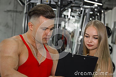 The trainer explains to the newcomer girl how to exercise on the in the gym. A pumped-up teacher helps a thin woman athlete to Stock Photo