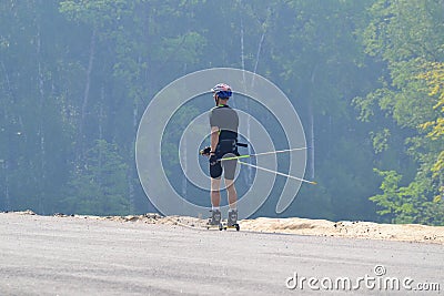 Training an athlete on the roller skaters. Biathlon ride on the roller skis with ski poles, in the helmet. Autumn workout. Roller Editorial Stock Photo