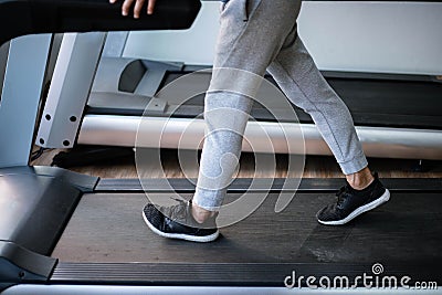 Training gym concept a male teenager wearing long pants and black trainers walking on a treadmill for cardio workout Stock Photo