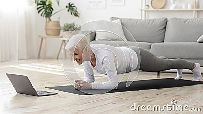 Sporty senior woman doing yoga plank while watching tutorial on laptop Stock Photo