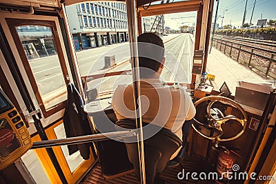 Tram driver in cabin of retro tramway moving vehicle past modern districts of capital city Editorial Stock Photo