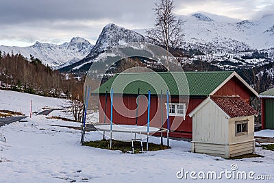 Trampoline and cozy wooden house in the Volda village; snow-covered mountains in the background Stock Photo