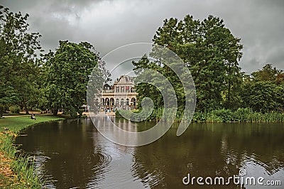 Tranquil lake with lawn, grove. building and cloudy sky in Amsterdam park. Editorial Stock Photo