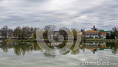 Tranquil landscape with lake, houses, cloudy sky, and trees reflected symmetrically in the water. Nyiregyhaza, Hungary Stock Photo