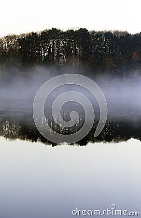 Tranquil Misty morning landscape of trees reflected in a still lake Stock Photo