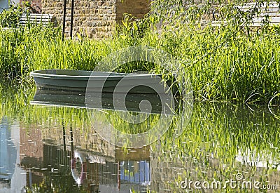 Tranquil river scene with empty rowing boat moored at the bank. Stock Photo