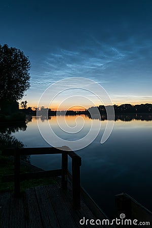 Tranquil scene after sunset near the calm water of a lake with shining night clouds NLC or noctilucent clouds in the sky Stock Photo