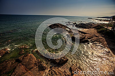 Turquoise Sea Waves Gleam under Sunlight Washing Rocky Beach Stock Photo