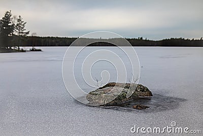 Tranquil winter scenery with a rock in frozen lake Stock Photo