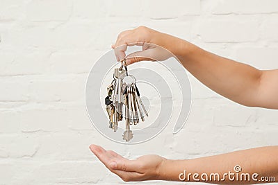 Transfer of house key on a white brick background. Woman's hands with bunch of keys Stock Photo