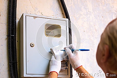 Transfer of readings of an electric meter. A man writes down the numbers of kilowatts Stock Photo