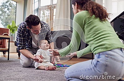 Transgender Family Encouraging Baby To Take First Steps In Lounge At Home Stock Photo