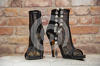 Translucent black summer women`s boots and white stone beads on a white leather banquette against a brick wall Stock Photo
