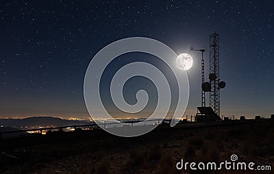 Transmission masts on a high mountain under a full moon with the illuminated coastline. Stock Photo