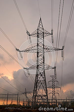 Transmission tower silhouette and high voltage overhead transmission lines, at sunset, with fiery orange skies and stormy clouds Stock Photo