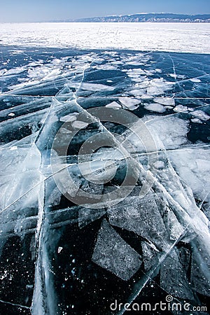 Transparent dark ice on Lake Baikal with frozen pieces of ice and large beautiful cracks. Stock Photo