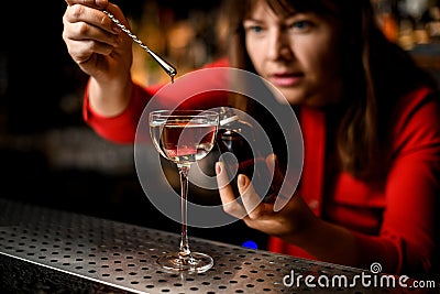 glass with liquid stands on bar and woman adds ingredient to it Stock Photo
