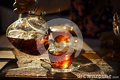 From transparent glass teapot pour black tea in glass mug, glows Stock Photo