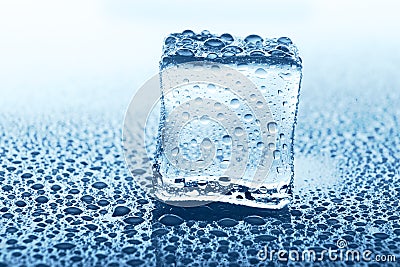 Transparent ice cube with reflection on blue glass with water drops Stock Photo