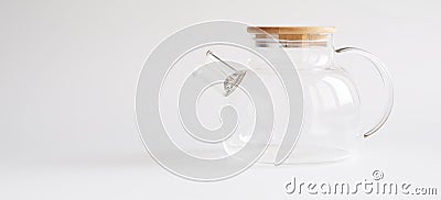 A transparent teapot made of tempered glass with a wooden lid and a metal spiral strainer on a white background. Element of modern Stock Photo