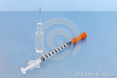 Transparent vial container with liquid medicine near small insulin syringe on blue background. Stock Photo