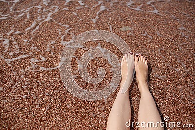 Travel concept - Woman's legs on beautiful tropical beach with pebble sand. Feet on sand and wave in summer time Stock Photo