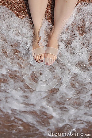 Travel concept - Woman& x27;s legs on beautiful tropical beach with pebble sand. Feet on sand and wave in summer time Stock Photo