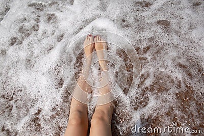 Travel concept - Woman& x27;s legs on beautiful tropical beach with pebble sand. Feet on sand and wave in summer time Stock Photo