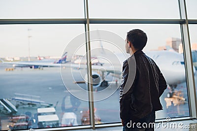 Travel concept with young man in airport interior with city view and a plane flying by. Stock Photo