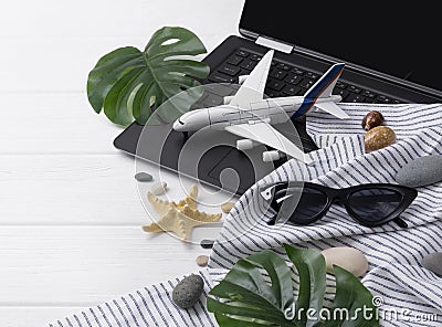 Travel flatlay: laptop, sunglasses, monstera leavs, plane, star fish and towel, shells, on wooden table with copy space Stock Photo