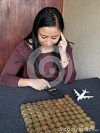 travel investment, brunette woman counting her savings with a figure of a white airplane and coins on the gray table Stock Photo