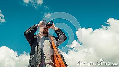 Travel Search Scout Concept. Hiking Man Looking Through Binoculars In The Distance Against The Sky. Low Angle Point Shoot Stock Photo