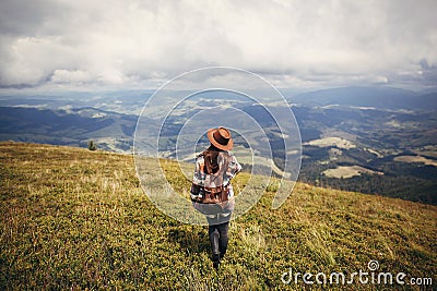 travel and wanderlust concept. stylish traveler hipster girl holding hat, with backpack and windy hair, walking in mountains in c Stock Photo