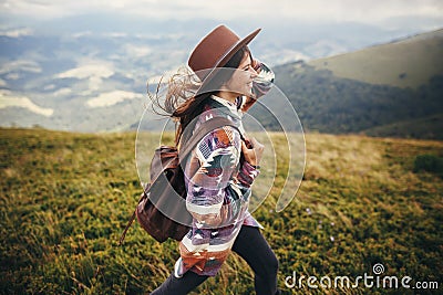 travel and wanderlust concept. stylish traveler hipster girl holding hat, with backpack and windy hair, walking in mountains in c Stock Photo