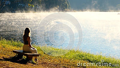 Travel woman relax on nature near misty lake. Female traveler sitting on bench Stock Photo