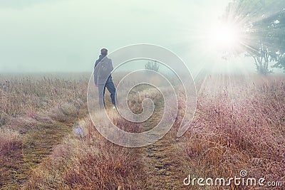 Traveler on autumn foggy meadow looks at on bright sunlight. Stock Photo