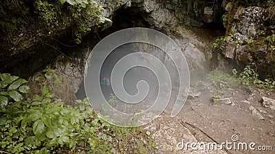 Traveler descends into cave. Stock footage. Explorer with insurance goes down steep descent into dark foggy cave in rock Stock Photo