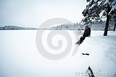 Traveler drinks hot drink by snowy lake Stock Photo