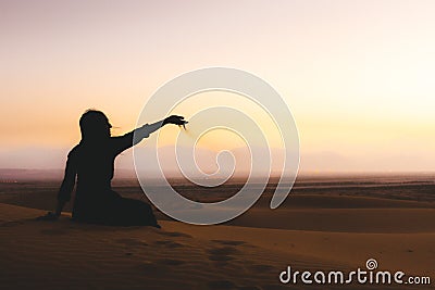 Traveler explorer girl sit in Desert and let sand fall from the hand.Silhouette of woman playing with sand on sunset in summer Stock Photo