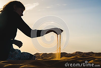 Traveler explorer girl sitting in the Sahara Desert and letting the sand fall from the hand, Morocco Stock Photo