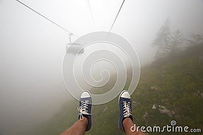Traveler ride mountain cableway stretching down over beautiful early autumn mountain landscape in deep fog. First person Stock Photo