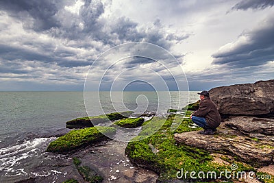 Traveler on a rocky seashore overgrown with green algae Stock Photo