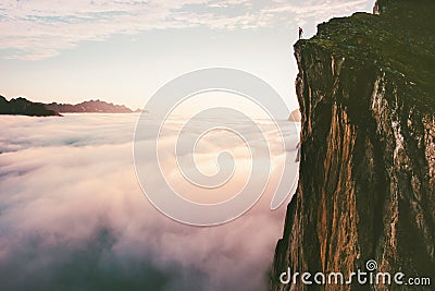 Traveler standing on cliff edge mountain top above sunset clouds Stock Photo